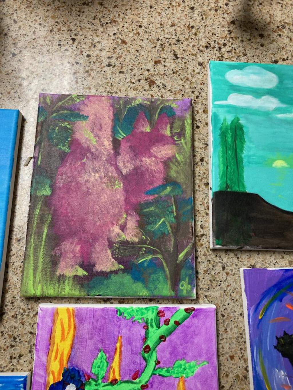 An acrylic painting depicts an abstract representation of what could be interpreted as the rear of a cat. The canvas is filled with hazy shapes in shades of purple, green, and pink, with subtle hints of blue and yellow that could suggest foliage or background elements. The color palette is vibrant and there seems to be a mix of brushstrokes, some of which give the impression of fur.